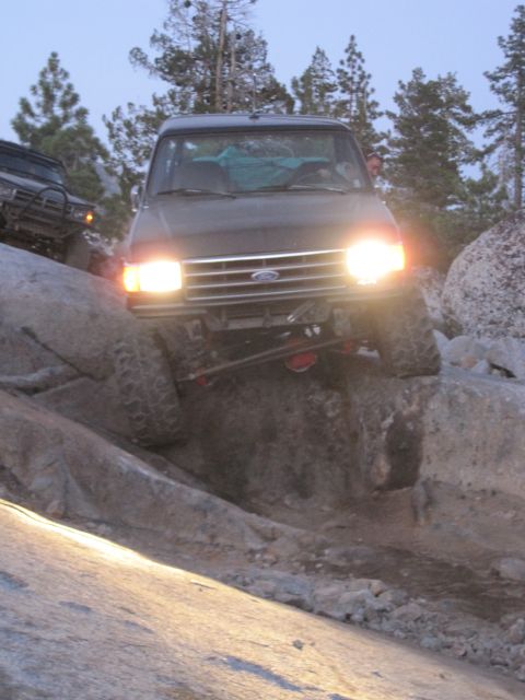 1989 Ford Bronco - This 1989 Ford Bronco is shown off-roading over rocks, with its headlights illuminating the path ahead.