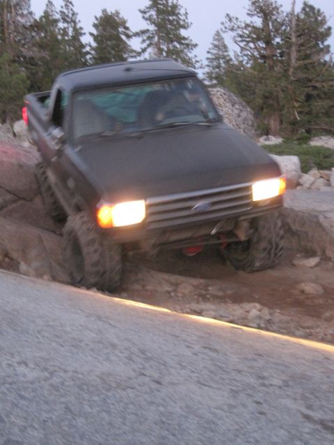 1989 Ford Bronco - A dark pickup truck with large tires is shown off-roading on a rocky path.