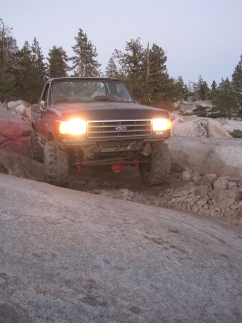 1989 Ford Bronco - Ford F-150 pickup truck navigates rocky terrain with headlights on.