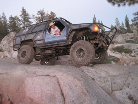 1989 Ford Bronco - A modified blue SUV navigates a rocky terrain with a driver wearing a hat.