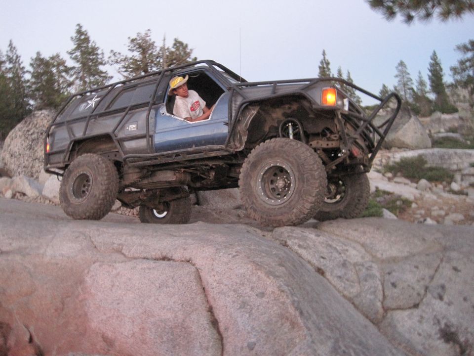Blue off-road SUV with roll cage and large tires climbing rocks