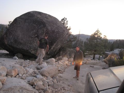 1989 Ford Bronco - Two men are in a rocky, wooded area near a very large boulder, with a vehicle partially visible in the foreground.