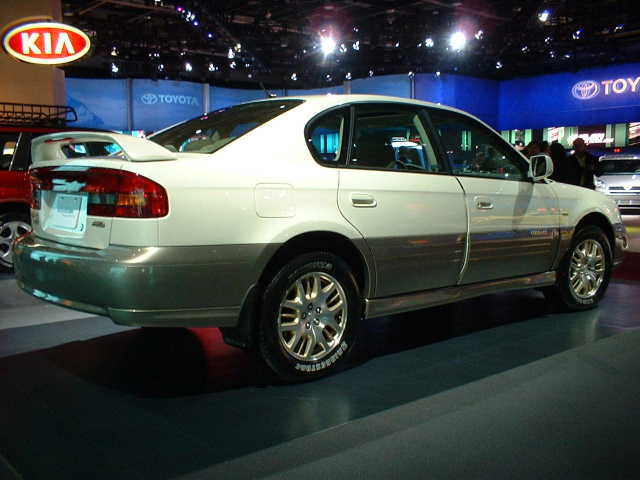 White sedan with a spoiler on the back, parked indoors with other cars and signs for Kia and Toyota