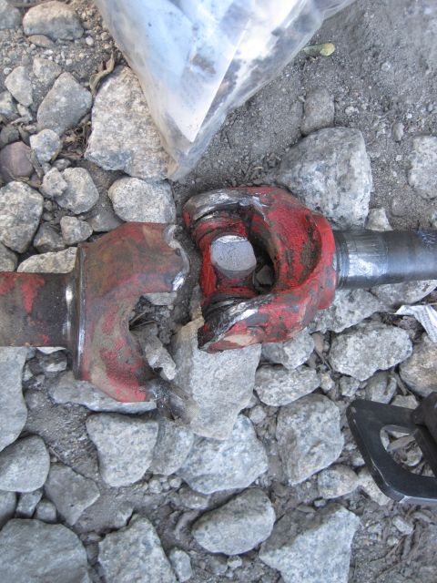 1989 Ford Bronco - A broken red driveshaft universal joint rests on a bed of gravel.