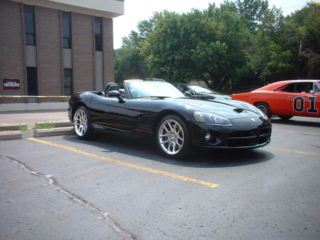 Black convertible sports car parked in a lot, with an orange General Lee car in the background
