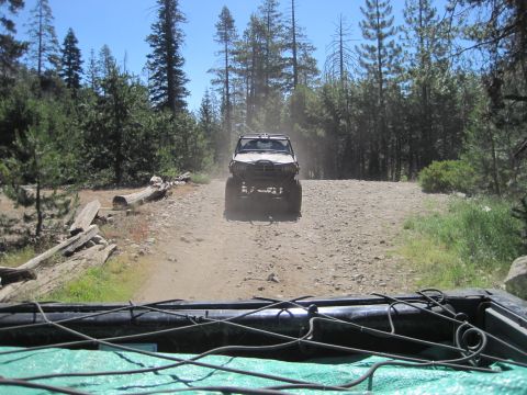1989 Ford Bronco - Two off-road vehicles travel on a dusty dirt road through a forest.