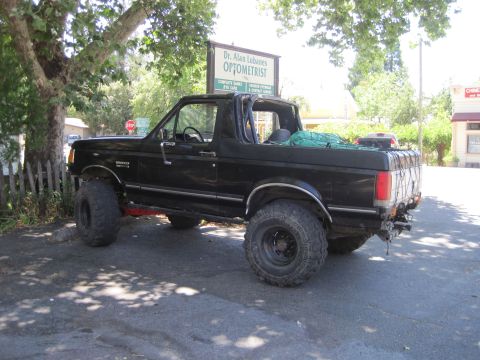1989 Ford Bronco - This lifted black Ford Bronco is parked on asphalt near a tree and a sign for an optometrist.