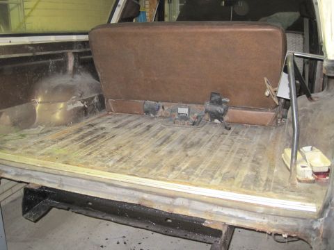 1979 Ford Bronco - The cargo area of a 1979 Ford Bronco shows its brown bench seat and the ribbed wood-paneled floor, indicating it is ready for restoration.
