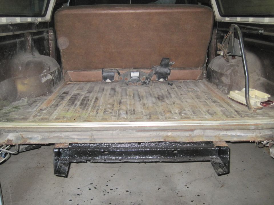 Interior cargo area with brown bench seat folded up, showing wooden floor and trailer hitch mechanism