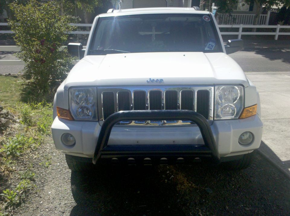 Front view of a white Jeep Commander SUV with black bull bar parked in a driveway