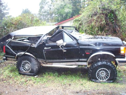 1990 Ford Bronco - This heavily damaged black Ford Bronco shows significant structural compromise to its roof and has flat tires.