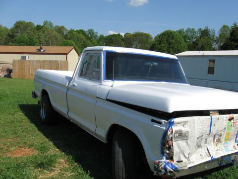 1995 Ford Bronco - A white pickup truck is parked on a grassy lawn with trees and buildings in the background.