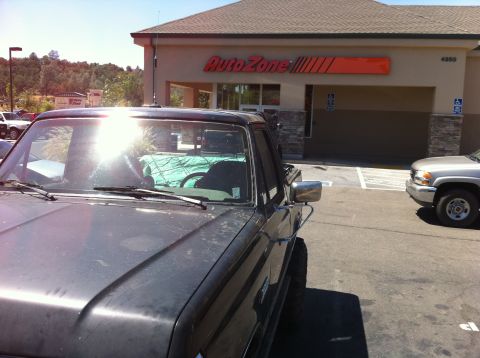 1989 Ford Bronco - A dark pickup truck is parked in front of an AutoZone store on a sunny day.