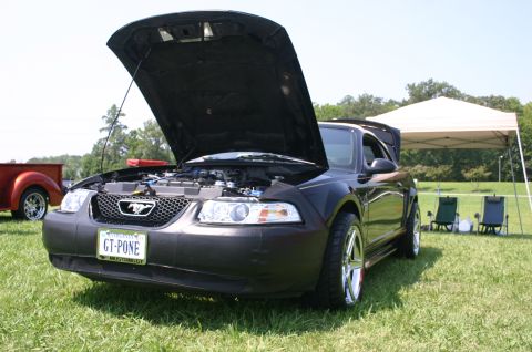 1968 Shelby GT500 - A dark-colored Ford Mustang is displayed with its hood open at an outdoor event.