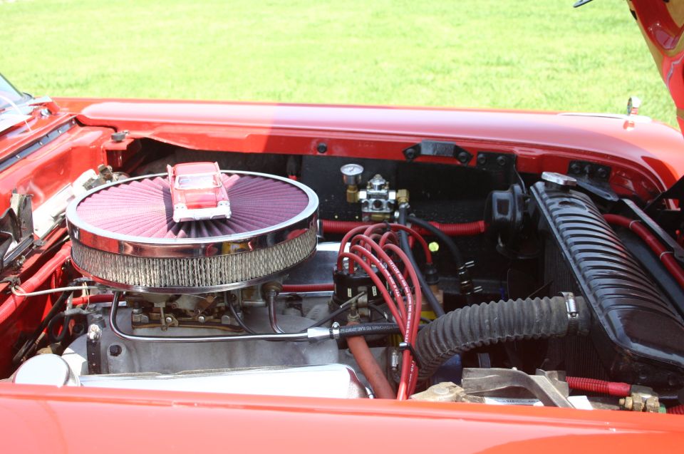 Red engine bay with chrome air filter housing topped by a red toy car, red spark plug wires, and a black radiator