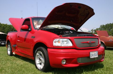 1968 Shelby GT500 - A red 1999 Ford F-150 SVT Lightning pickup truck is displayed with its hood open at a car show.