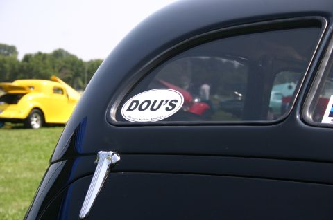 1968 Shelby GT500 - A sticker on the rear window of a black car, with a yellow hot rod visible in the background.