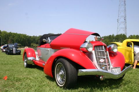 1968 Shelby GT500 - A red and silver convertible is displayed with its hood open at a car show, with other vehicles visible in the background.
