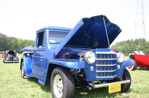 1968 Shelby GT500 - Blue pickup truck at a car show, hood open, with other vehicles in the background.