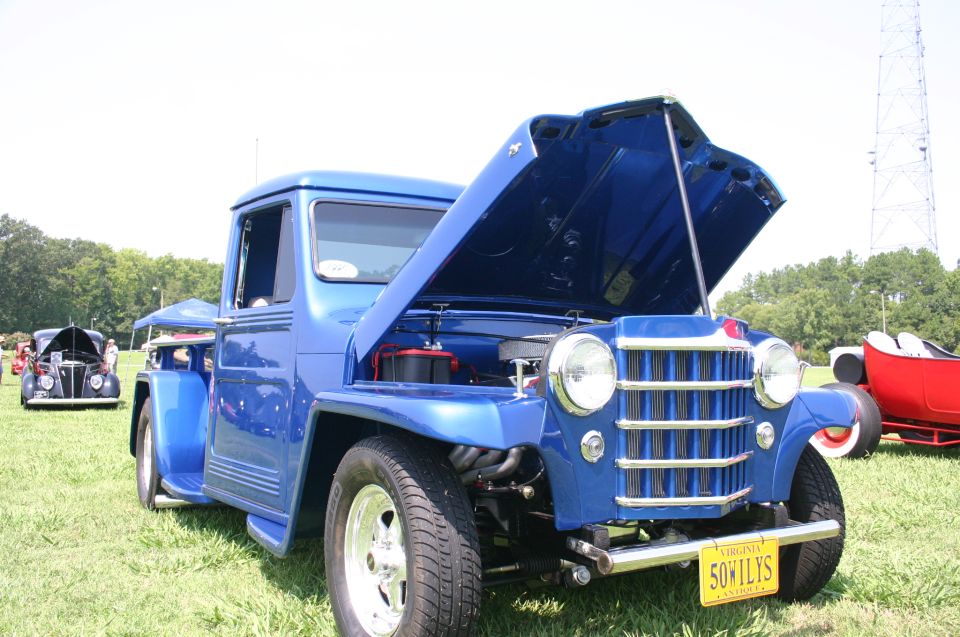 Blue pickup truck, hood open, showing engine. Virginia license plate reads '50WILYS'. Another car visible in background