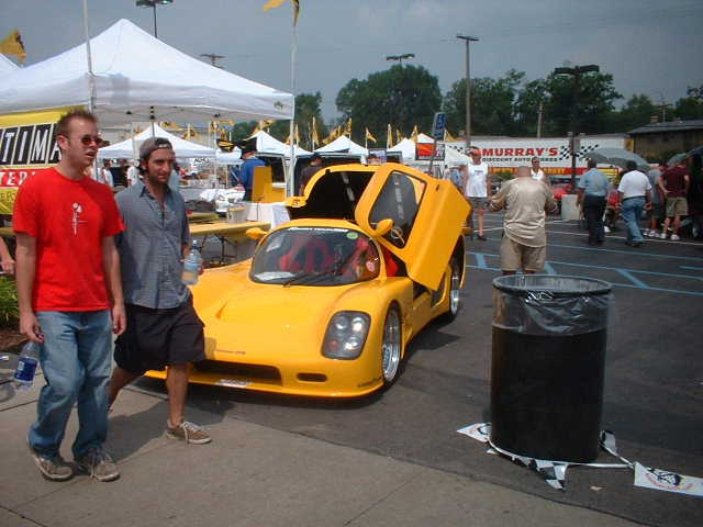 Yellow sports car with doors open, two guys standing nearby. Trash can in foreground