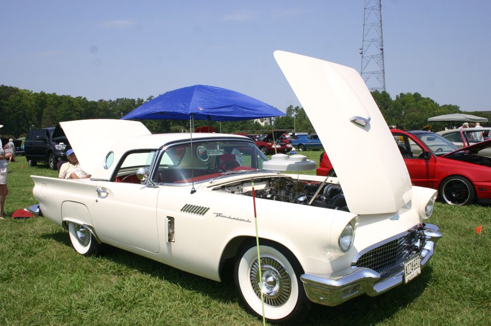 White 1957 Ford Thunderbird with hood open, red interior, wire wheels, and a blue canopy