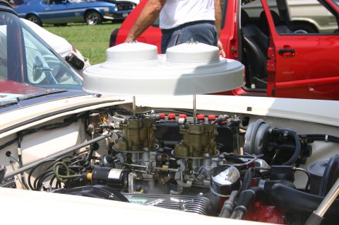 1968 Shelby GT500 - Close-up view of a car's engine bay dual carburetors and a prominent air cleaner, with other vehicles visible in the background.