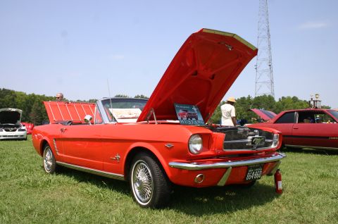 1968 Shelby GT500 - A red 1965 Ford Mustang convertible is displayed with its hood open at a car show, with another car visible in the background.