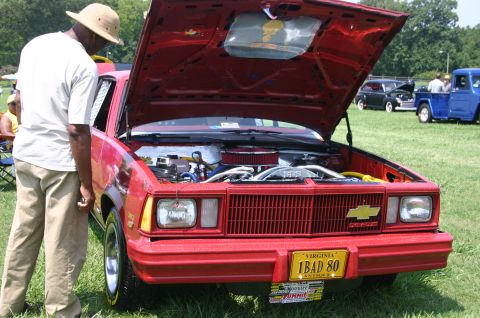 1968 Shelby GT500 - A red Chevrolet with its hood open is displayed at a car show, with other vehicles visible in the background.