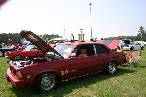 1968 Shelby GT500 - Red coupe with hood open at a car show, displaying trophies and other vehicles in the background.