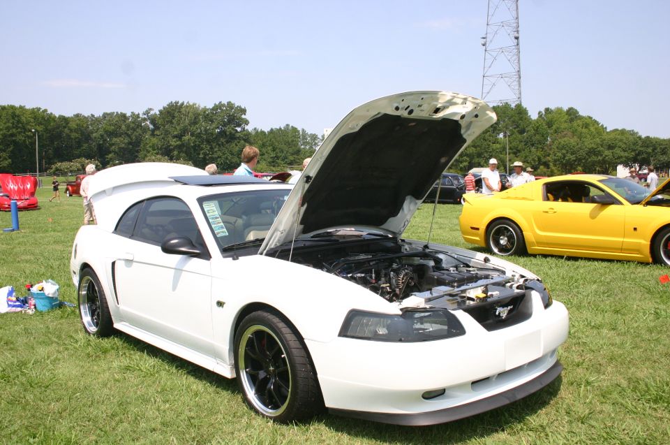White Ford Mustang with hood and trunk open, black wheels, sunroof. Yellow Mustang in background