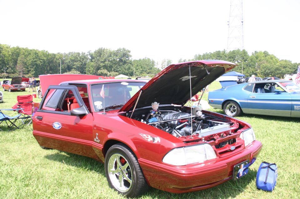 Red 1987 Ford Mustang GT with hood open, showing engine. Blue 1971 Ford Mustang Mach 1 in background