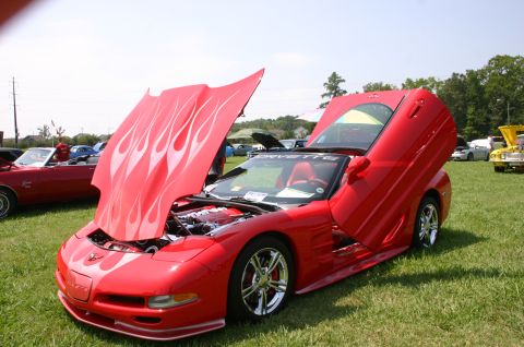 1968 Shelby GT500 - A red sports car with custom flame decals on the hood and upward-swinging doors is displayed at a car show.