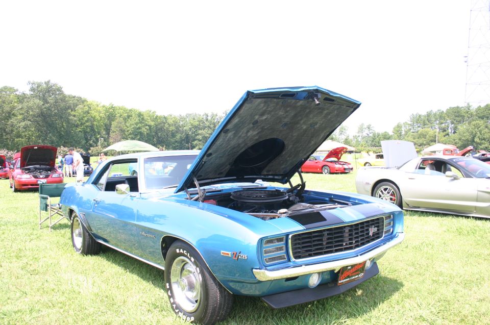 Blue 1969 Camaro with hood open, parked on grass at a car show. Other cars and people in background
