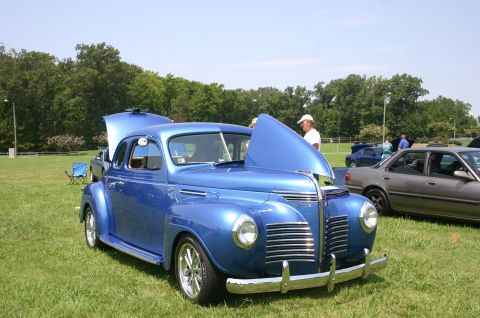 1968 Shelby GT500 - A blue sedan from the 1940s is displayed with its hood open at a car show.