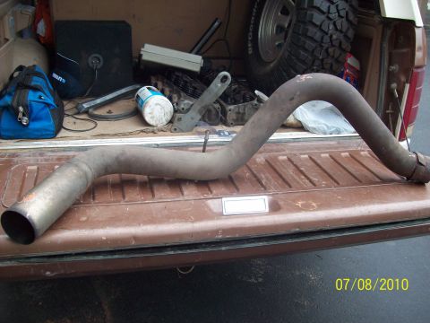 1985 Ford Bronco - An exhaust pipe is laid out in the bed of a truck, alongside other vehicle parts and a spare tire.