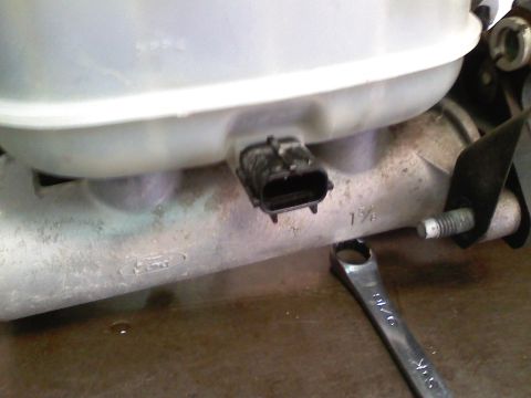 1990 Ford Bronco - Close-up of a brake master cylinder reservoir and sensor with a wrench nearby.