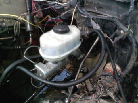 1990 Ford Bronco - The brake master cylinder and associated plumbing are visible amidst a complex network of wires and hoses in the engine compartment.