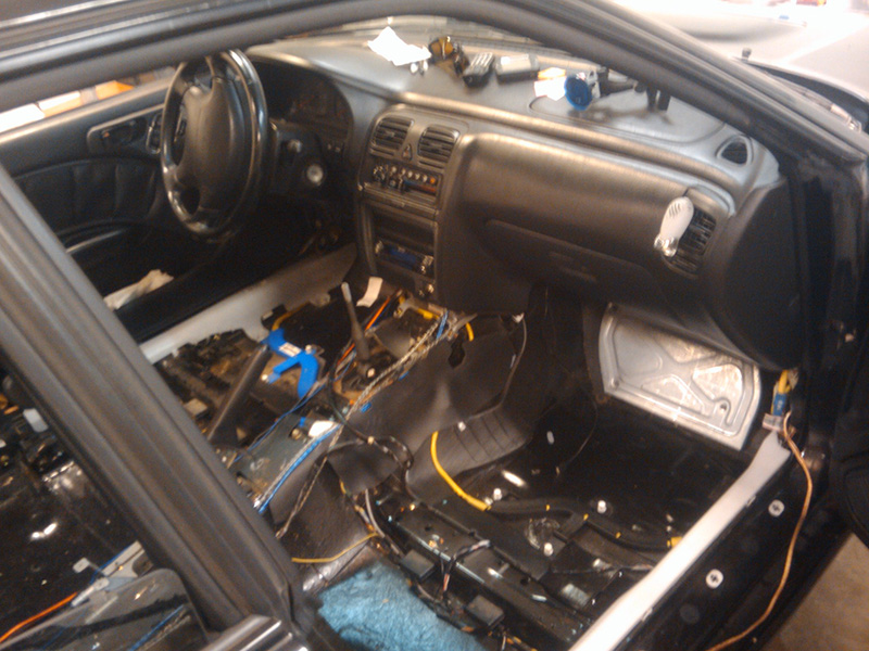 1998 Subaru Legacy interior with dashboard, steering wheel, and center console visible; floor stripped bare with exposed wiring and insulation