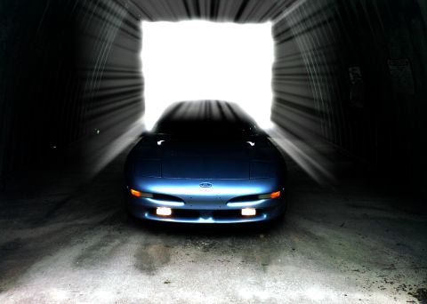 1994 Ford Probe - A blue 1994 Ford Probe is seen from the front as it emerges from a brightly lit tunnel.