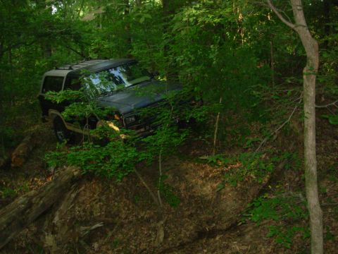 1983 Ford Bronco - Jeep Cherokee XJ navigating a steep, wooded incline with fallen logs.