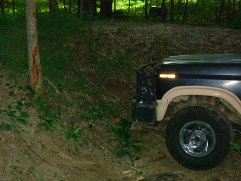 1983 Ford Bronco - A dark blue and tan Ford Bronco is parked on a dirt path in a wooded area.
