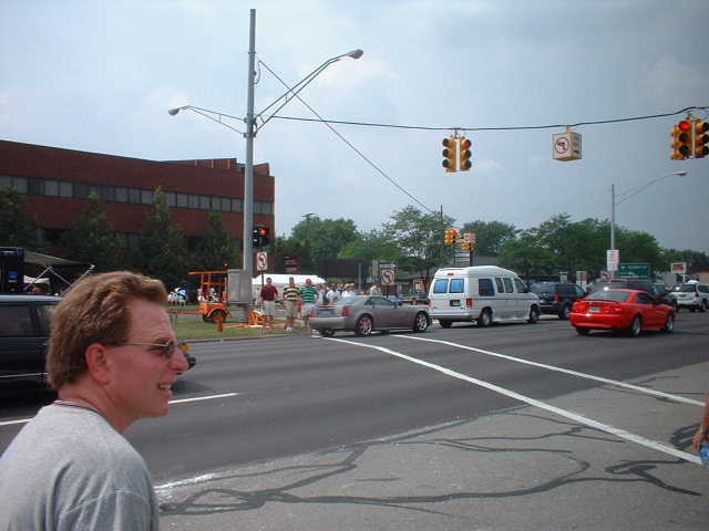 Man in foreground, cars and people on street, buildings in background