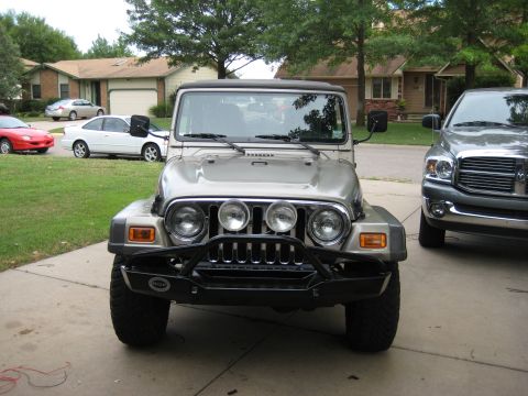 2005 Jeep Wrangler - This silver Jeep Wrangler is shown from the front, an aftermarket bumper and auxiliary lights, parked next to a pickup truck.