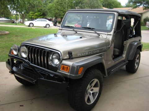 2005 Jeep Wrangler - Driver-side 3/4 front view of a khaki Jeep Wrangler Unlimited with doors removed and the black soft top folded back, parked on a driveway.…