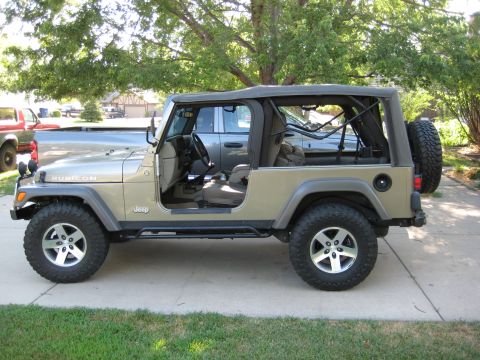 2005 Jeep Wrangler - Driver-side profile of a khaki long-wheelbase Jeep Wrangler Unlimited with the doors removed and the tan soft top folded back, showing the…