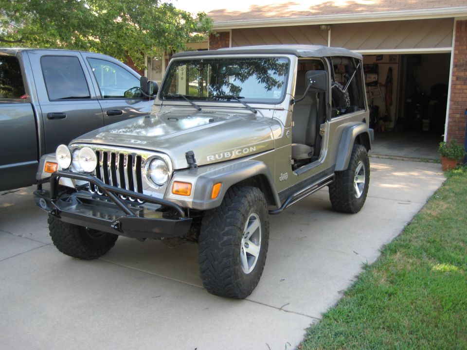 Silver 2005 Jeep Wrangler Rubicon with aftermarket bumper and off-road tires parked next to a gray pickup truck