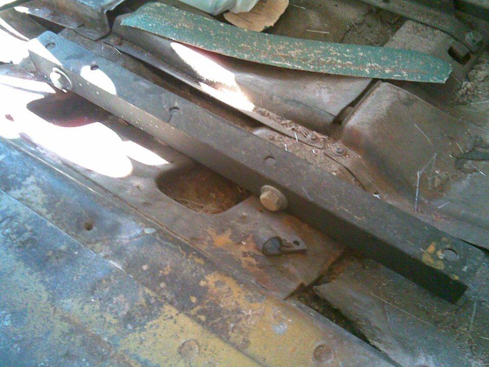 Underside view of a rusty leaf spring and frame rail with hardware on a vehicle