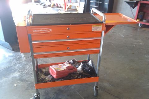 2000 Mercury Grand Marquis - An orange tool cart with a blue point logo sits on a concrete floor, holding various items in its drawers and lower shelf.