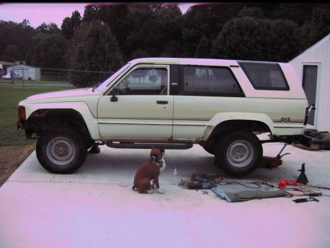 1992 Ford Mustang - A cream-colored Toyota 4Runner is parked on a concrete surface, appearing to undergo maintenance with a jack supporting the rear.